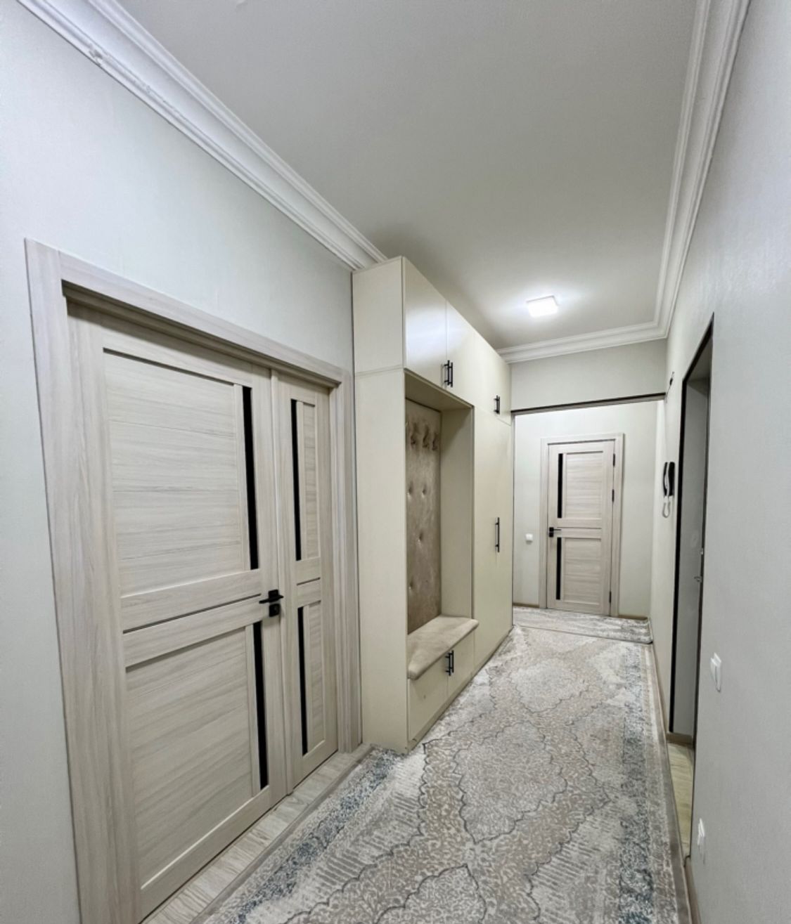 A hallway with white doors, a bench, and a patterned carpet.