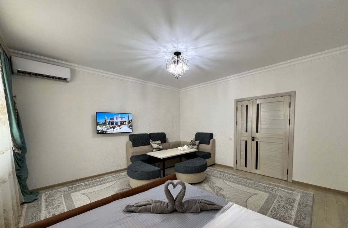 A hotel room with a bed, a chandelier, a television, a sofa, and a dining table.