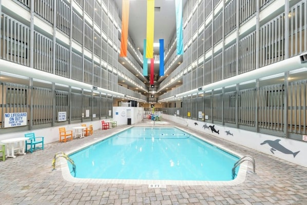 Una piscina interior con suelo de baldosas, barandillas metálicas y coloridos banderines verticales.
