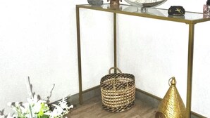 A room with a glass-top table, a woven basket, a decorative bowl, a small statue, a dreamcatcher, and a wall-mounted mirror.
