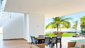 A modern interior with a dining area, a sofa, and a poolside view.
