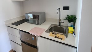 A compact kitchen with a built-in microwave, stainless steel sink, and a refrigerator.