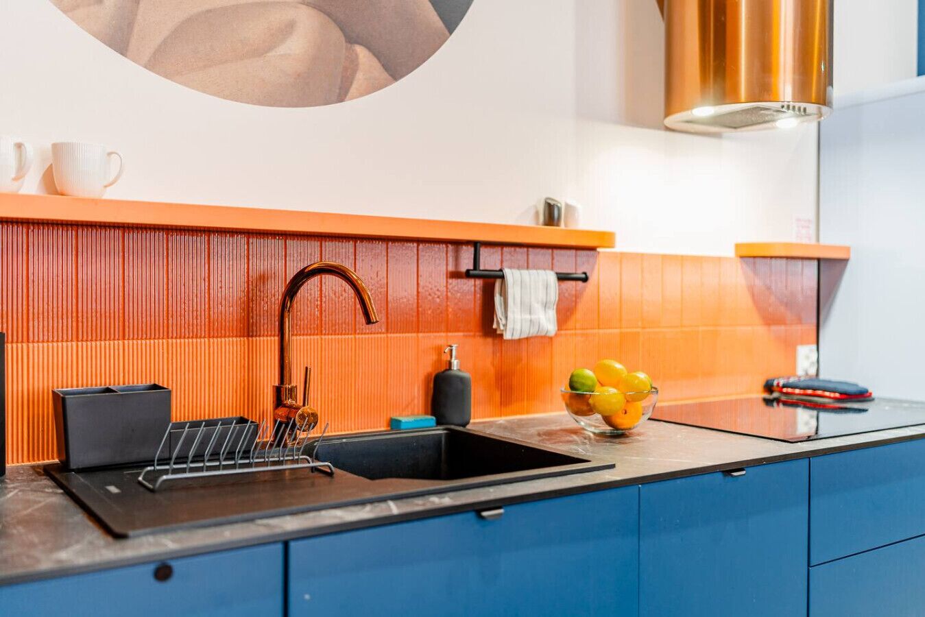 A modern kitchen with a black sink, orange backsplash, and blue cabinets.