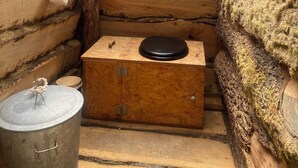 A rustic wooden cabin interior with a wooden bench, a metal bucket, and a small wooden box.