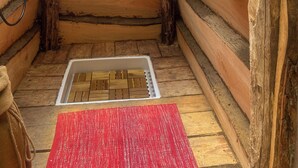 A log cabin interior with a wooden floor, a red mat, a white vent, and a wooden shelf.