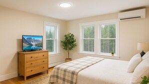 Un dormitorio con cama, cómoda, televisor, ventanas y una planta.