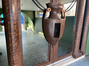 A large, rustic-looking metal urn with chains, placed in a doorway with green walls and tiled floor.