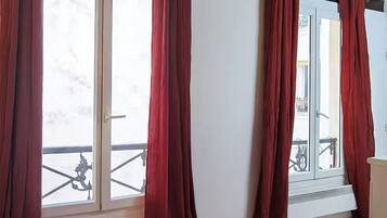 A room with large windows covered by red curtains, a wooden floor, and a visible balcony with a railing.