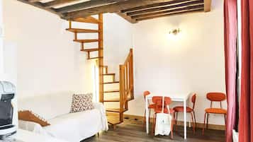 A cozy room with a white sofa, a wooden staircase, and a dining area with orange chairs.