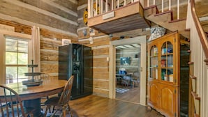A rustic cabin interior with a wooden dining table, chairs, a black refrigerator, a wooden cabinet, and a staircase.