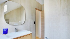 A modern bathroom with a large oval mirror, a white sink, and wooden cabinetry.