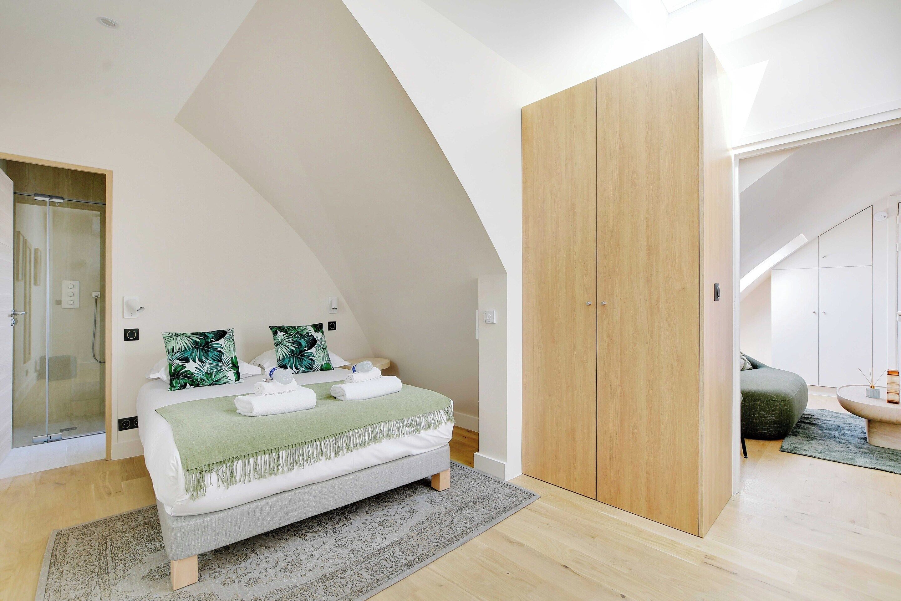 A bedroom with a bed, a wooden wardrobe, a shower, and a glass door.