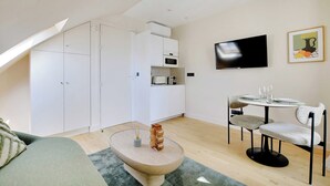 A modern, well-lit room with a dining area, kitchenette, and a TV mounted on the wall.