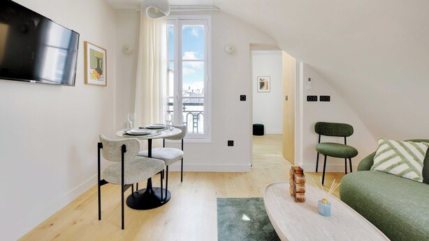 A modern, well-lit apartment with a dining area, a living room, and a view through a large window.