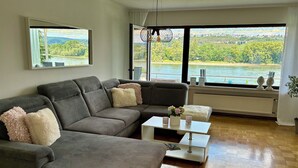 Een moderne woonkamer met een grijze modulaire bank, een witte salontafel en uitzicht op een rivier en een brug.