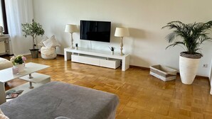 Een moderne woonkamer met een grijze bank, een witte tv-meubel en twee potplanten.