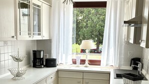 Een keuken met witte kasten, een kroonluchter, een koffiezetapparaat en een raam met gordijnen.