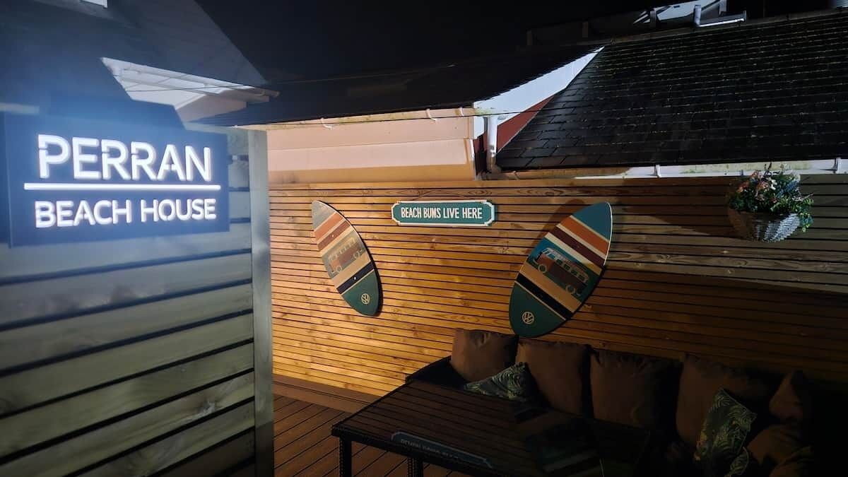 A beach-themed interior with a sign reading 'PERRAN BEACH HOUSE' and another sign stating 'BEACH BUMS LIVE HERE'.