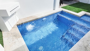 En rektangulär swimmingpool med klart, blått vatten, omgiven av en betongplattform och en liten yta med konstgräs.