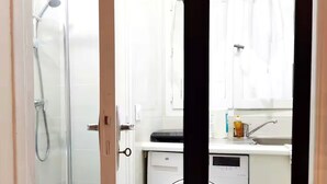 A compact bathroom with a shower, a washing machine, and a sink with a soap dispenser.
