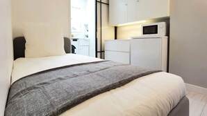 A modern hotel room with a bed, a small kitchenette with a microwave, and a sliding door leading to a balcony.