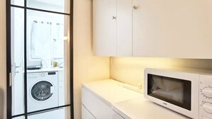 A compact laundry room with a washing machine, a microwave, and a small countertop with a sink.