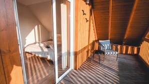 Um deck de madeira com uma cama e uma cadeira, porta de vidro deslizante e teto inclinado.