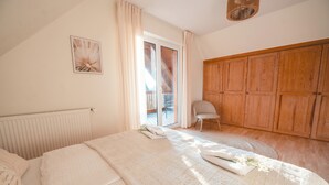 Quarto com cama, uma cadeira, guarda-roupa de madeira e janela com cortinas.