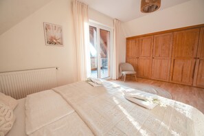A bedroom with a bed, a chair, a wooden wardrobe, and a window with curtains. - FachWerkPerle at Alfsee (Rieste)