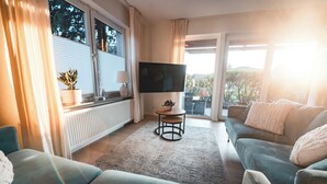 Uma sala de estar com sofá, televisão, mesinha e planta em vaso.