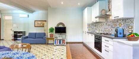 A modern kitchen with white cabinets, a tiled backsplash, and a dining area with a patterned tablecloth.