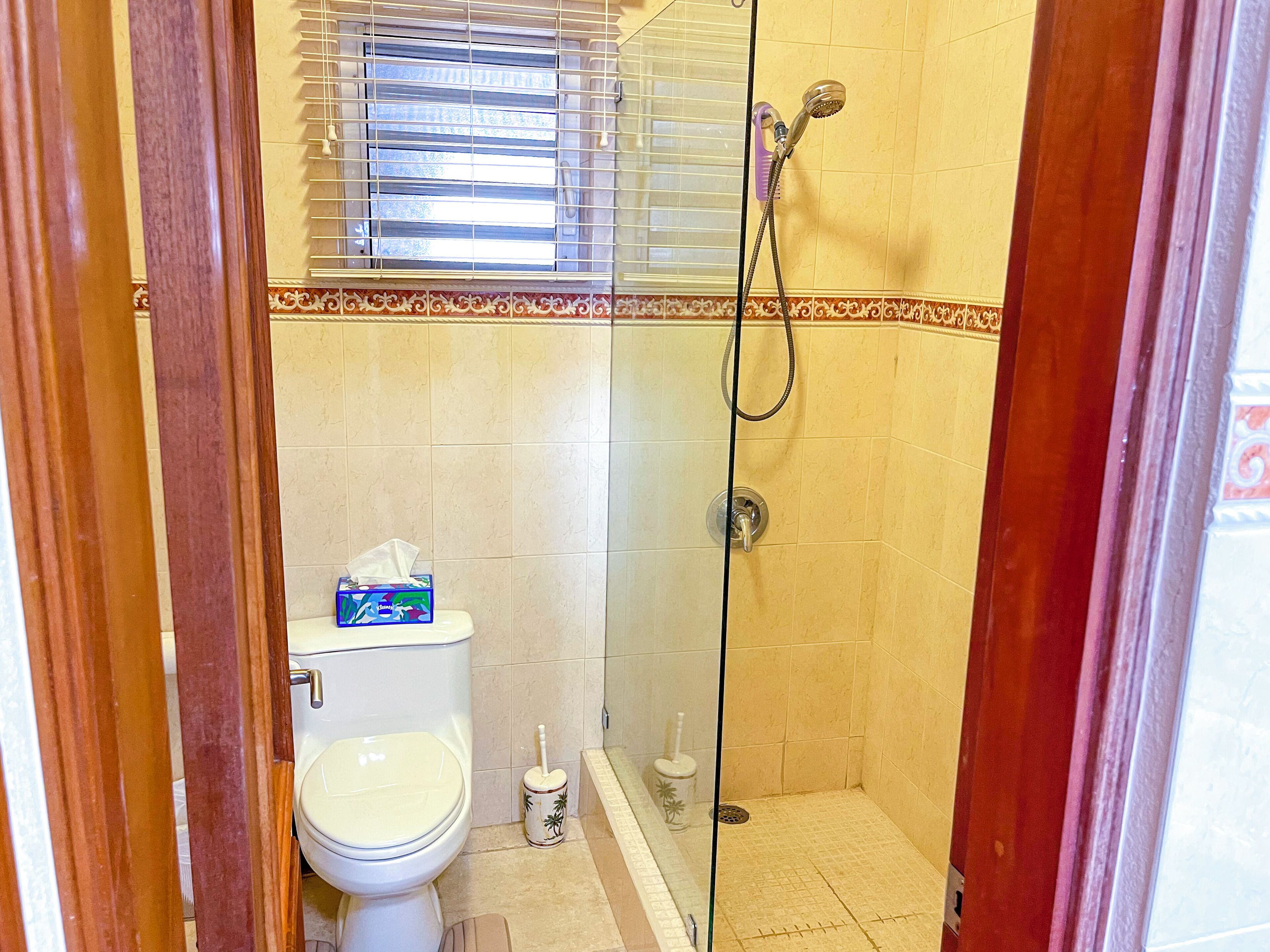 A small bathroom with a toilet, a shower, and a window with blinds.