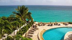 Zwembad van een resort met ligbedden en parasols, met uitzicht op een turquoise zee.