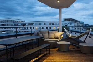 A rooftop terrace with a hammock, seating area, and a view of the cityscape.