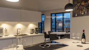 Een moderne keuken met een centraal eiland, een eethoek met een tafel en stoelen, en uitzicht op buiten door grote ramen.