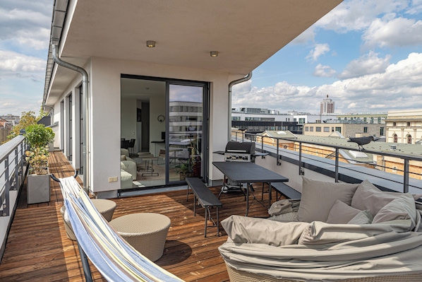 A balcony with a wooden deck, outdoor furniture, and a view of the cityscape.