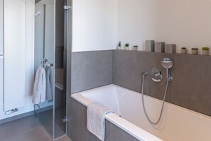 A modern bathroom with a glass shower enclosure, a white bathtub with a handheld showerhead, and a towel rack with towels.