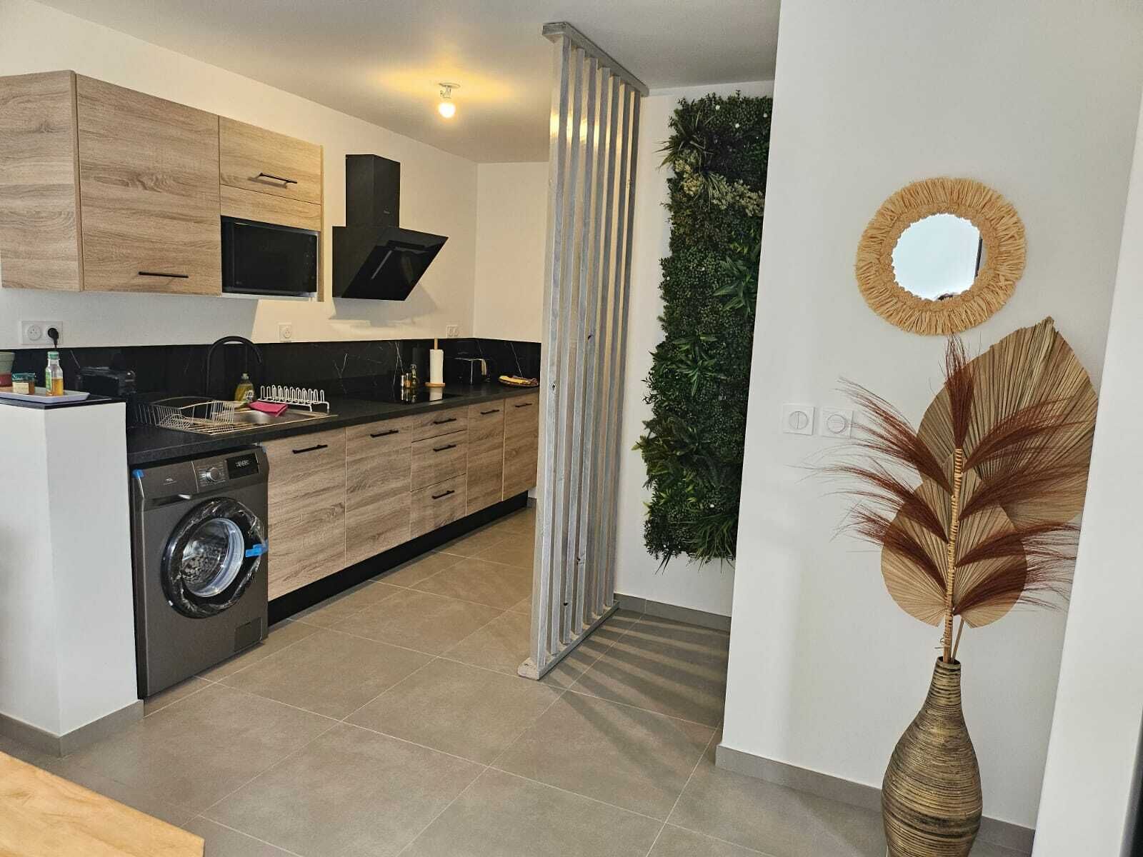 A modern kitchen with a built-in washing machine, a vertical garden, and a decorative vase.