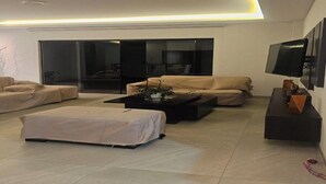 A modern living room with a sofa, ottoman, and coffee table, a sliding glass door leading to a balcony, and a flat-screen TV mounted on the wall. - one-bedroom apartment (Cochabamba)