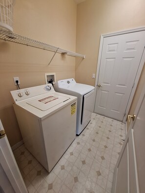 A laundry room with two washers and dryers, a metal shelf, and a white door. - Luxury Villa - Family Oasis with Private Pool - close to Disney and Universal! (Clermont)