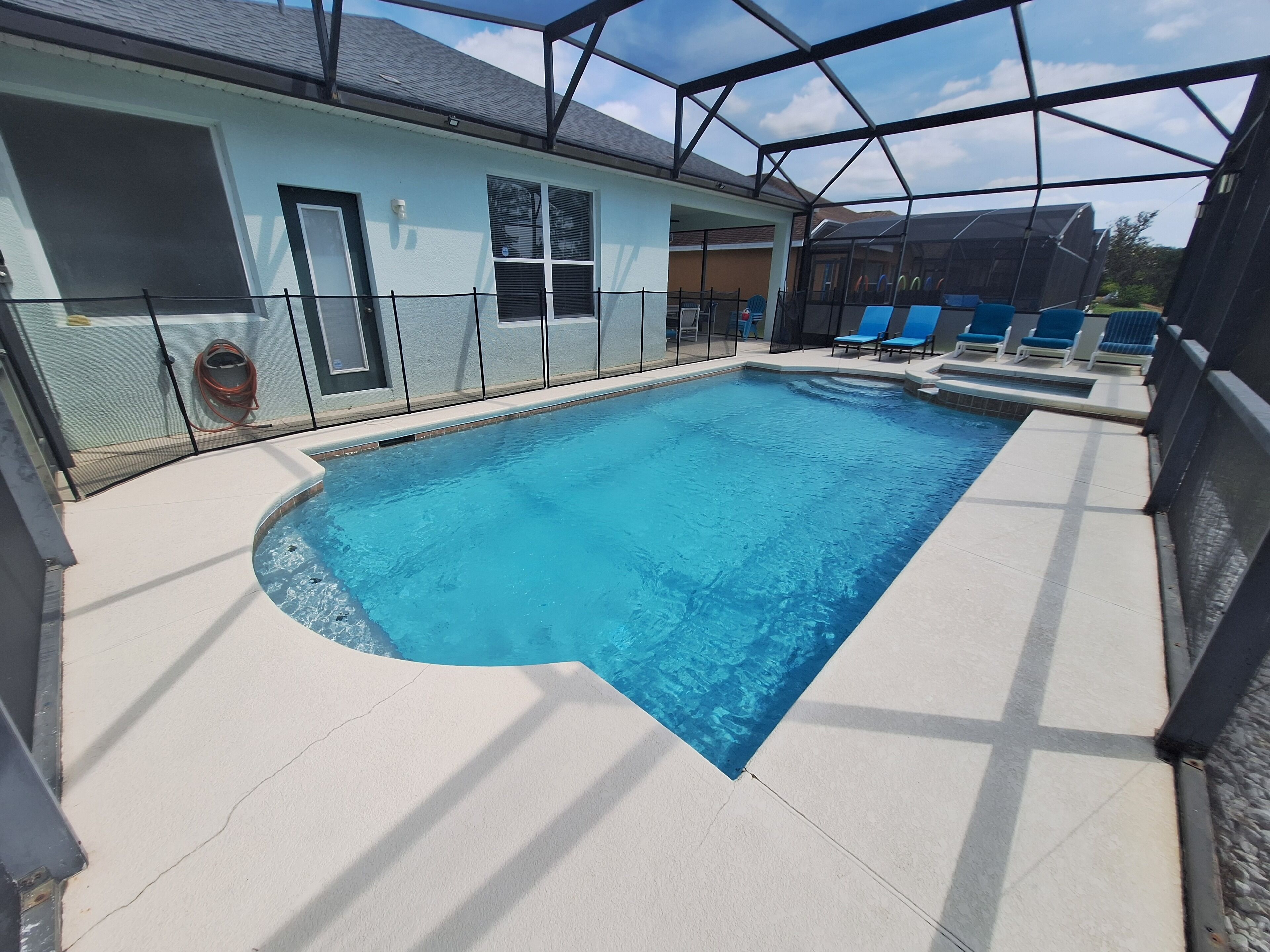 A swimming pool with a sunshade structure, surrounded by lounge chairs and a covered area with a view of the landscape.
