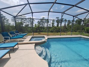A covered outdoor swimming pool with blue lounge chairs and a hot tub.