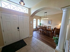 A dining area with a wooden table and chairs, a black doormat, and a large window with a view. - Luxury Villa - Family Oasis with Private Pool - close to Disney and Universal! (Clermont)