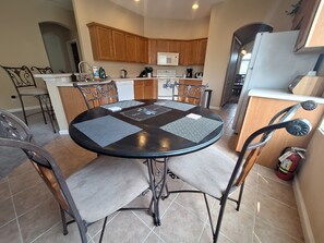 A dining area with a round table, four chairs, and a kitchen in the background.