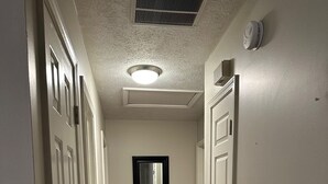 A hallway with wooden flooring, white walls, and a ceiling vent.