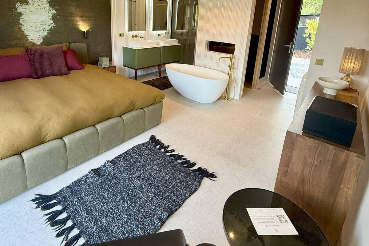 A modern bedroom with a large bed, a sitting area, a bathtub, and a small table.