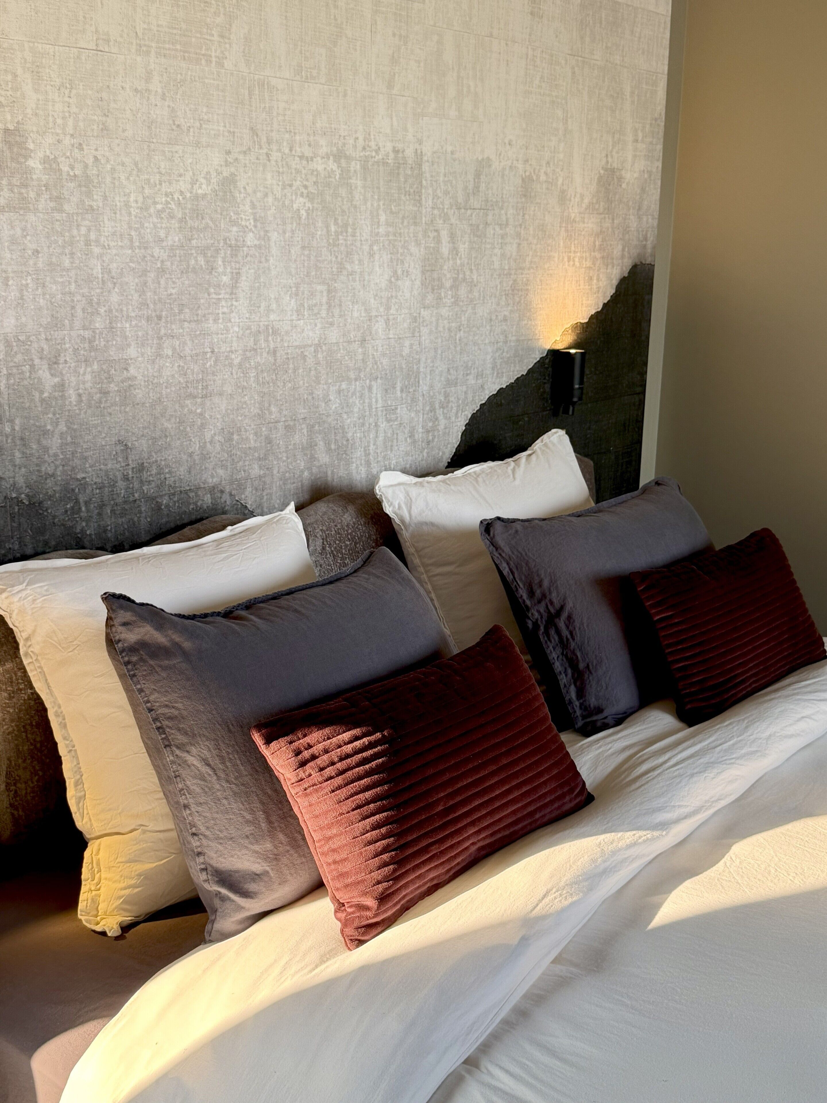 A bed with multiple pillows and a textured wall behind it.
