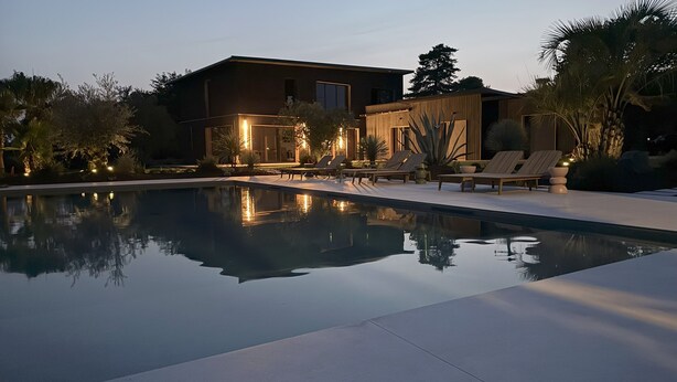 Une maison moderne dotée d’une piscine, de chaises longues et d’espaces extérieurs bien éclairés.