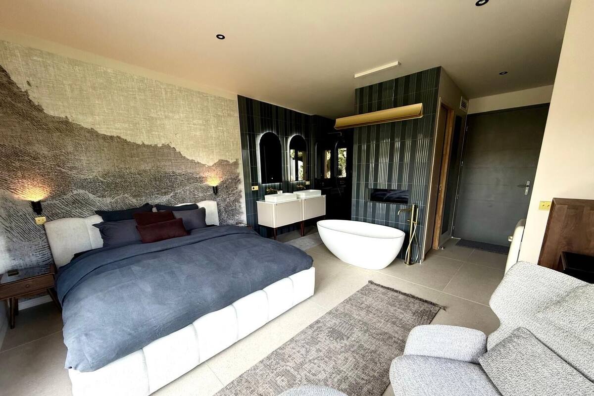 A modern bedroom with a large bed, a built-in vanity, and a bathtub.