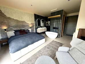 A modern bedroom with a large bed, a built-in vanity, and a bathtub.